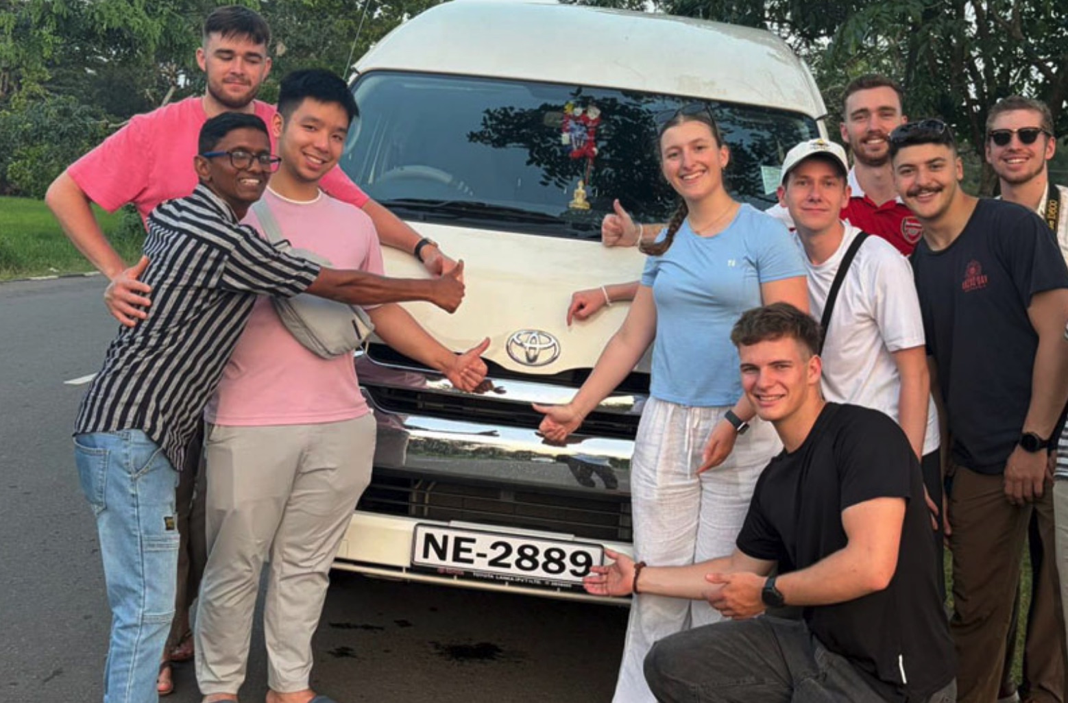 A group of travellers with their private driver beside a white charter van in Sri Lanka