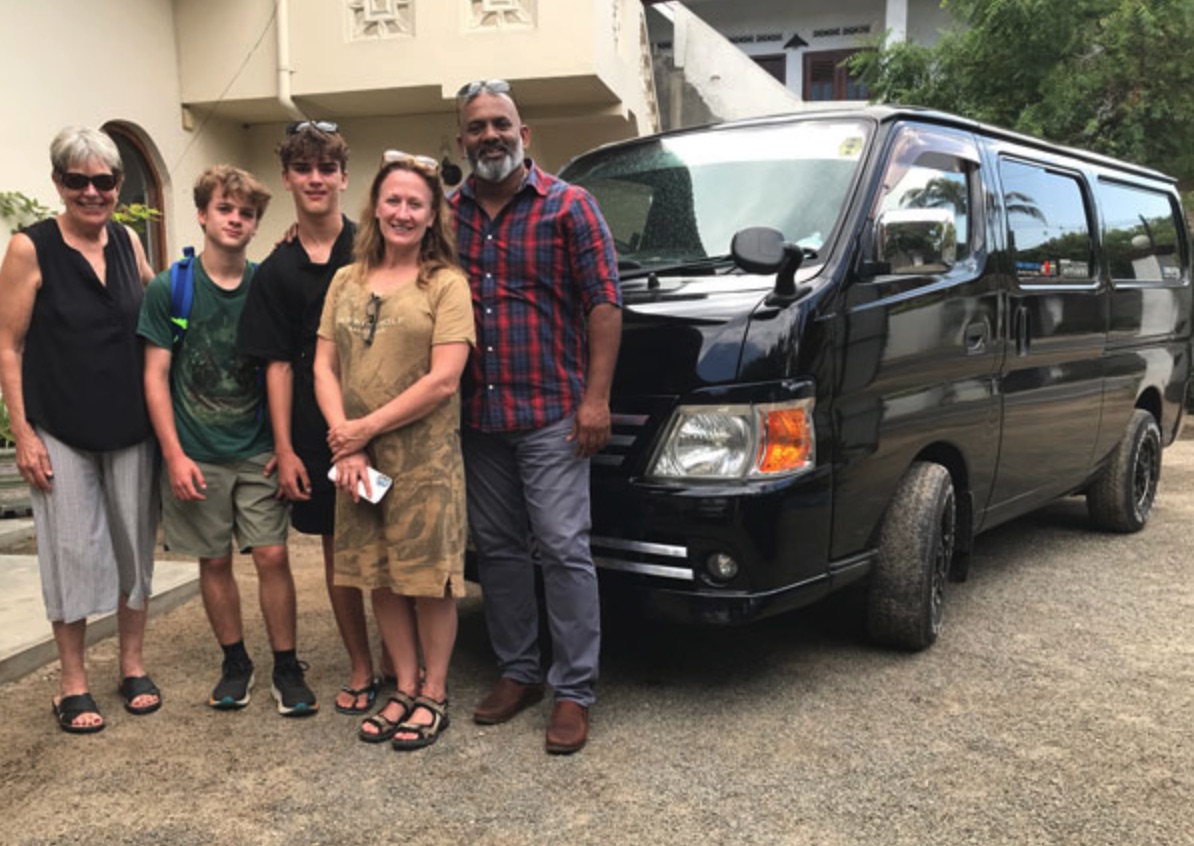 A family with teenagers and their private driver beside a black charter van in Sri Lanka
